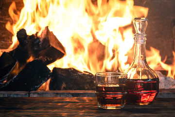 Strong alcohol in a transparent bottle and a drinking glass on a wooden table on a burning fire...
