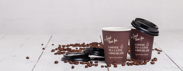 Paper cup of coffee and coffee beans on white wooden background