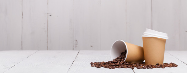 Paper cup of coffee and coffee beans on white wooden background