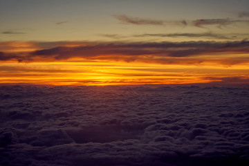 orange sky and clouds from an airplane window during an evening flight.