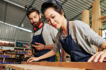 Smiling Vietnamese female carpenter working with wood under control of coworker