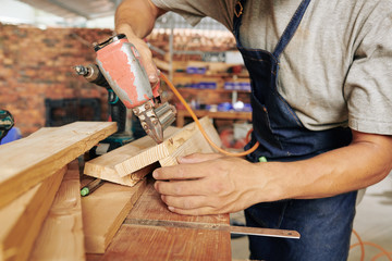 Close-up image of professional carpenter using staple gun when working with wood in his studio