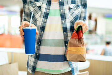 person holding a fast food package and glass with lunch in public
