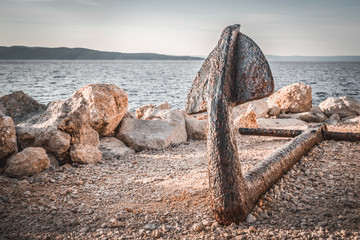 Old rusty anchor on the beach with stones