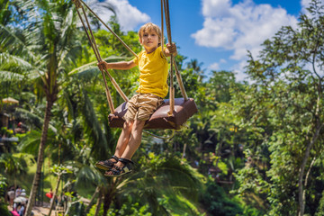 Young boy swinging in the jungle rainforest of Bali island, Indonesia. Swing in the tropics. Swings - trend of Bali. Traveling with kids concept. What to do with children. Child friendly place