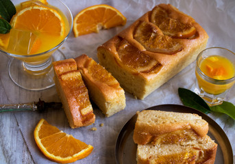 fruchtiger rührkuchen mit orangenscheiben belegt, mit einem glas orangensaft und einem orangenlikör