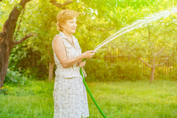 female gardener pouring plants in the garden with water hose
