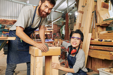 Multi-ethnic team of cheerful carpenters working on wooden stool in workshop