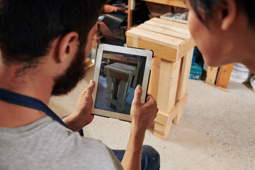 Carpenters making photo of wooden stool they made on tablet computer to upload it in online store