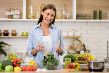 Happy woman cooking dinner, mixing fresh salad in kitchen