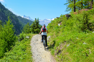 Fototapeta premium Young man riding bicycle in beautiful hilly landscape of Swiss Alps close to famous Zermatt. Outdoor sport. Bike, biker. Alpine landscape, Switzerland. Mountains with snow on top in background