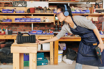 Smiling female carpenter tuning on speaker before starting to work with wood