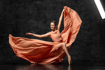 Ballerina. A young ballet dancer dressed in a long peach dress, pointe shoes with ribbons. The girl performs an elegant, graceful dance movement. Beautiful classic ballet. Advertising ballet studio.