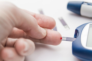 Man takes blood from the finger using the test strip for checking blood sugar level by blood glucose meter. Diabetes concept. Lancet pen and test strips on the background. Closeup, selective focus