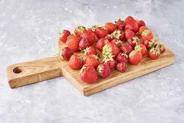 Heap of fresh strawberries with cutting board on a gray background, top view. Healthy nutrition