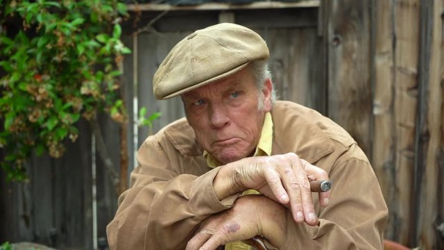 Portrait of old grumpy man holding cigar and leaning on his cane, looking off to the side, unhappy and disgruntled