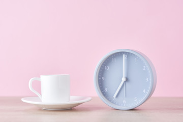 Classic gray alarm clock and white coffee cup on a pink background