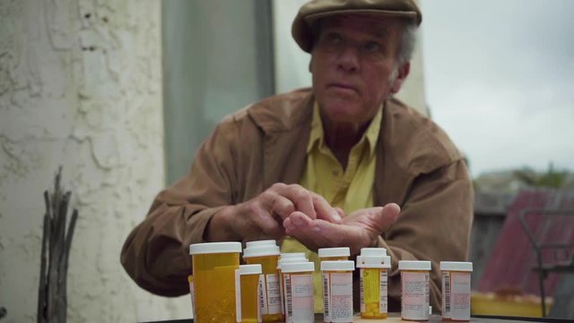 Elderly man counts his pills and medication with difficulty, looking up to sky in confusion; concept aging process