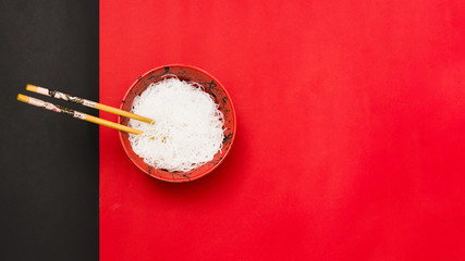 High angle view of white vermicelli in bowl with chopsticks over dual backdrop