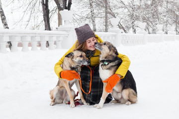 Portrait of beautiful smiling young woman with her two dogs in a snowy winter park.