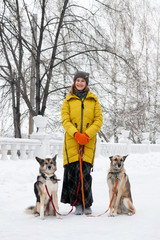 Portrait of beautiful smiling young woman with her two dogs in a snowy winter park.