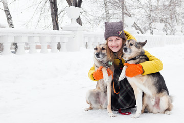 Portrait of beautiful smiling young woman with her two dogs in a snowy winter park.
