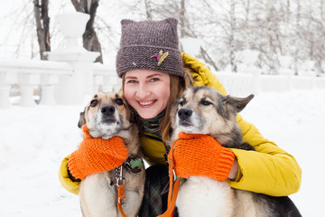 Beautiful smiling young woman with her two dogs in a snowy winter park.