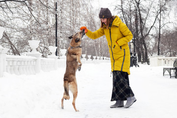 Beautiful smiling young woman is playing with her dog in a snowy winter park.