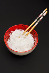 Rice vermicelli in bowl with chopstick over black surface