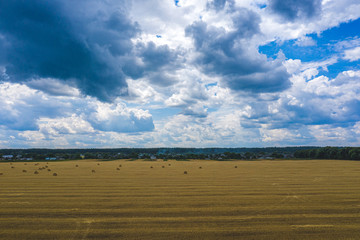 Aerial Flying over field with blue cloudy sky, rain, Straw bales in fields