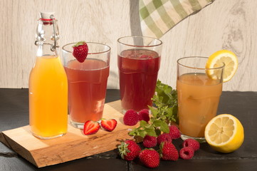 erfrischendes getränk in flasche und glas mit erdbeeren himbeeren zitrone melisse und eiswürfel auf schieferplatten und holzbrett