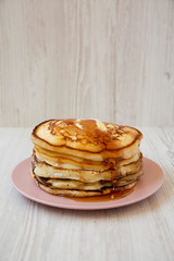 Homemade pancakes with butter and maple syrup on a pink plate, side view. Close-up.