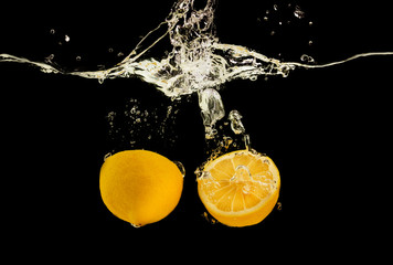 Cut lemon falling deeply under water with bubbles