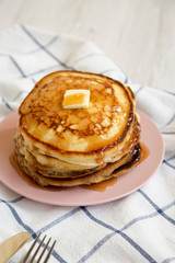 Homemade pancakes with butter and maple syrup on a pink plate, low angle view.