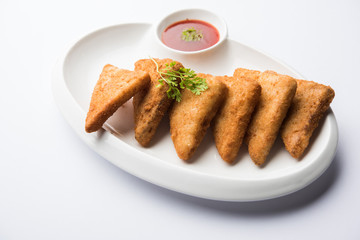 crispy Potato triangles or batata vada covered with bread crumbs and then deep fried. served with tomato ketchup. selective focus