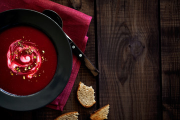 Traditional vegetarian red beet soup or smoothie decorated with chopped pistachios and sour cream in the black plate on a dark wooden background in rustic style top view with copy space for text