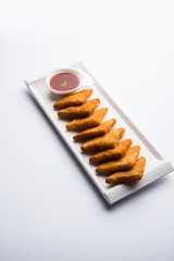 crispy Potato triangles or batata vada covered with bread crumbs and then deep fried. served with tomato ketchup. selective focus