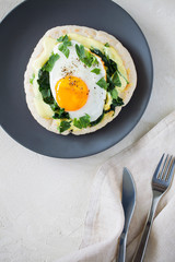 Healthy gourmet homemade spiced fried eggs with Indian spices, sauteed spinach and parsley used to top toasted pitas spread with turmeric yogurt on gray plate close-up top view with copy space