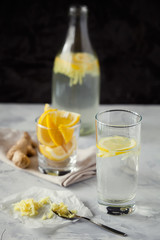 Homemade refreshing infused detox water or lemonade in glass bottles with grated ginger and lemon on dark background close-up with copy space for text.Healthy vegan drink concept.Selective focus
