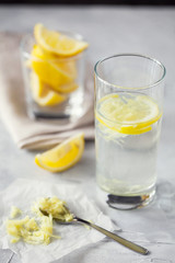 Homemade refreshing infused detox water or lemonade in glass with grated ginger and lemon on grey background close-up.Healthy vegan drink summer concept.Selective focus