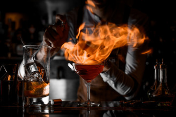 Professional male bartender putting fire from the lighter on the cocktail glass