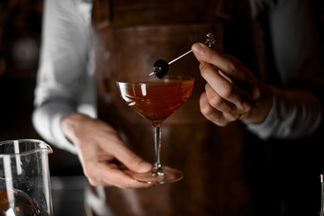 Bartender serving a cocktail in the glass decorated with berry on the skewer
