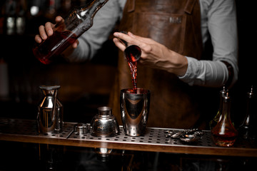 Bartender pouring an alcoholic drink from the steel jigger to the cocktail shaker