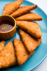 crispy Potato triangles or batata vada covered with bread crumbs and then deep fried. served with tomato ketchup. selective focus