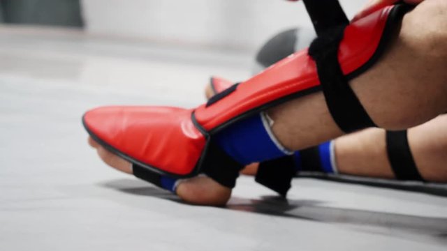 Close up athlete boxer man fighter in sportswear tying bandage shield on legs before boxing. Fighter wearing red leg shield. Kickboxer man preparing for boxing practice at gym.