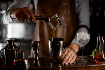 Fototapeta na wymiar Bartender putting a big ice cube with tweezers to the steel shaker