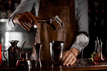 Male bartender putting a big ice cube with tweezers to the steel shaker