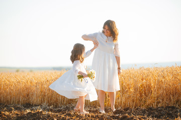 Photo of a little girl and a woman, wearing white dress, dancing and having fun in a wheat field