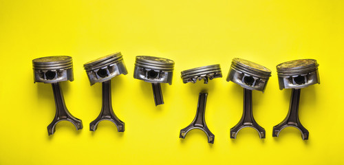 Old broken pistons and connecting rods on yellow background