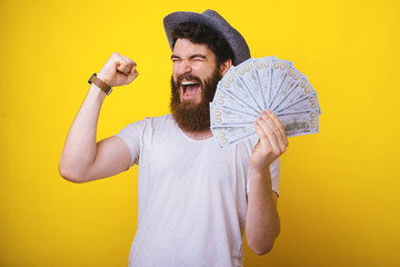 Photo of bearded guy,  standing overr yellow background, celebrating hi s triumph, holding a lot of...